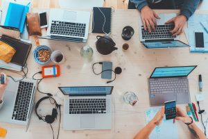 Aerial view of people sitting at laptops around a table and using phones and other peripherals.