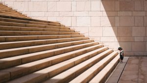 A toddler, looking down at the first step, stands at the base of a staircase