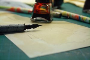 Photograph of a fountain pen on a sheet of drawing paper and next to a glass bottle of ink.