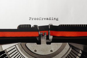 A typewriter with a red-and-black ribbon. The word "Proofreading" is centered on an otherwise blank page.