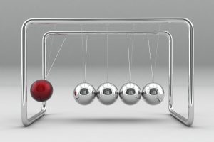 A Newton's cradle featuring four silver balls and one red ball. The silver balls are at rest, touching each other. The red ball is suspended in mid-swing to their left.