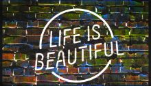 A neon sign against a brick wall. The sign reads "LIFE IS BEAUTIFUL" in all capital letters.