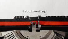 A typewriter with a bright-red ribbon. The word "Proofreading" is centered on an otherwise blank page.